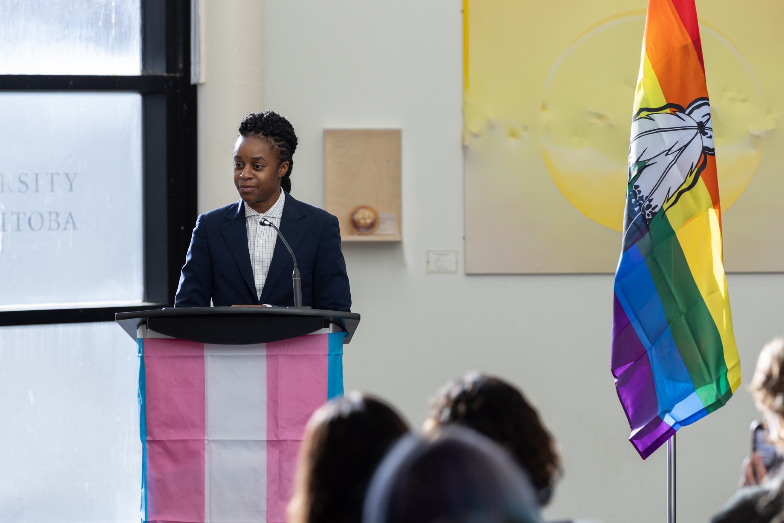 Uzoma Asagwara speaks at a podium that is adorned with a trans flag.