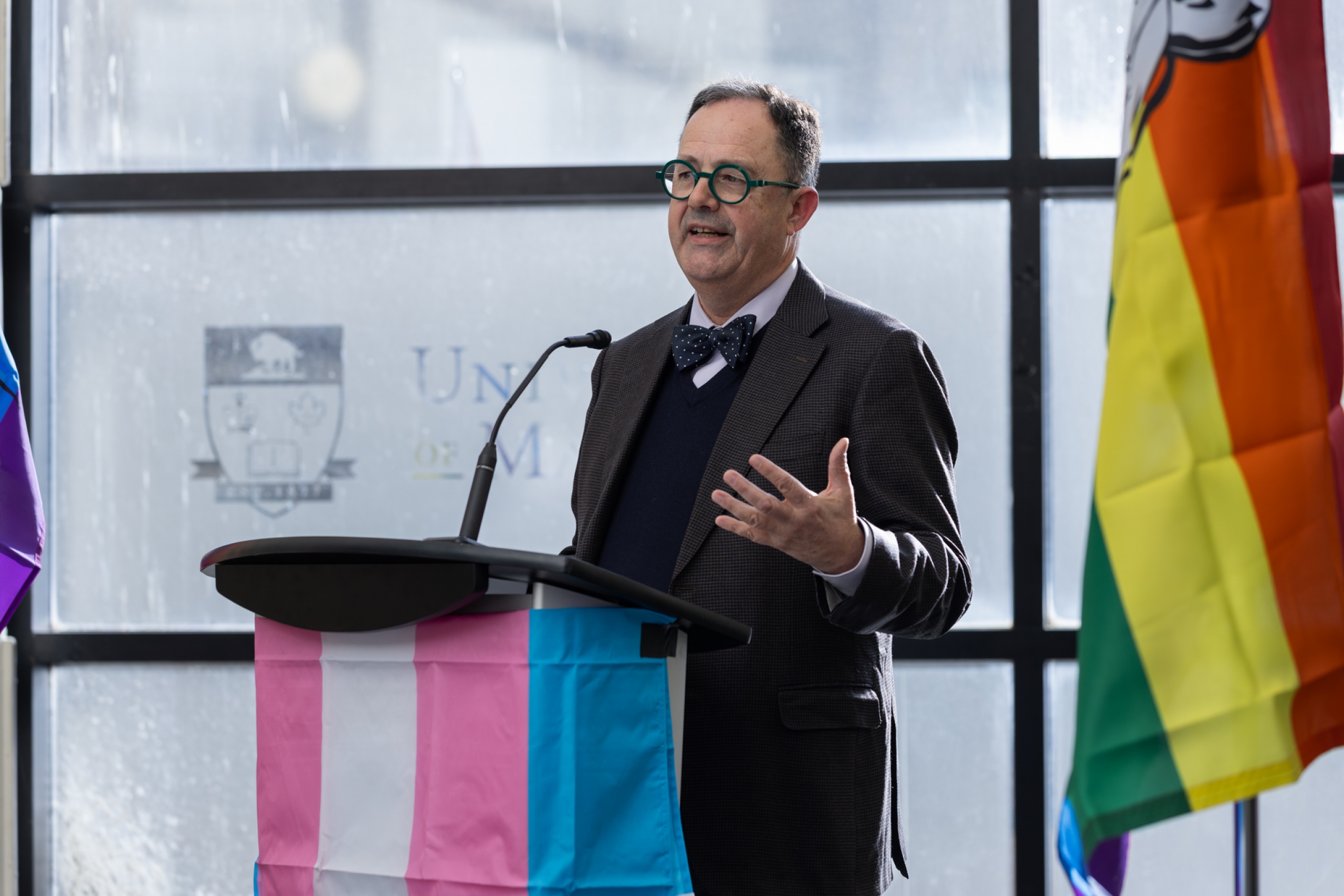 Dr. Peter Nickerson speaks at a podium adorned with a trans flag.