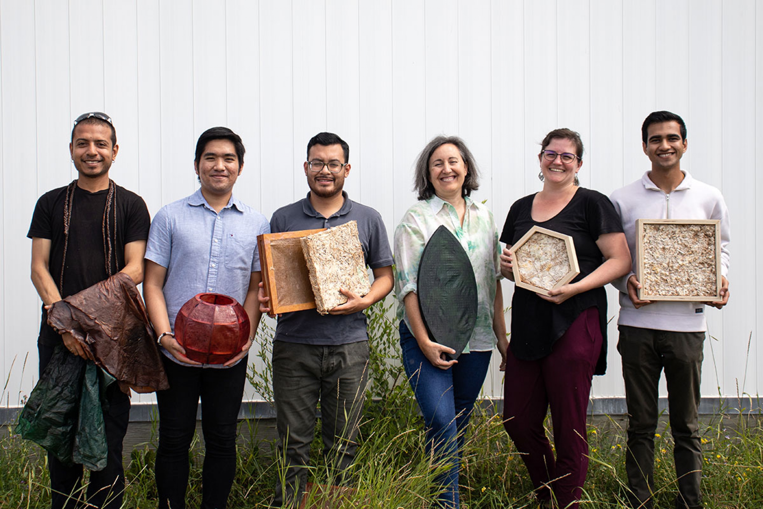 Six people standing in a row holding various building materials.