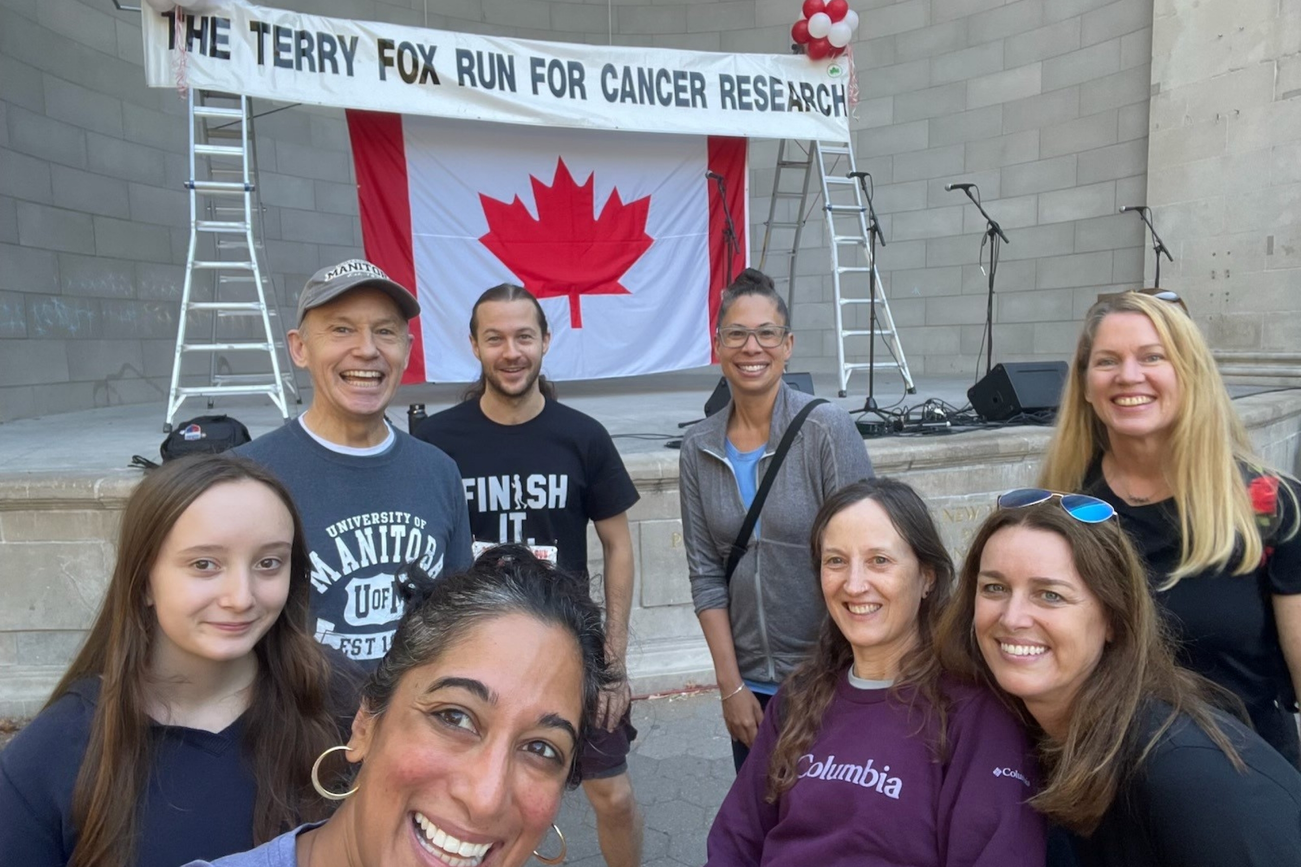 A group of people standing in front of a Canadian flag and a banner that reads 'Terry Fox run for cancer research.'