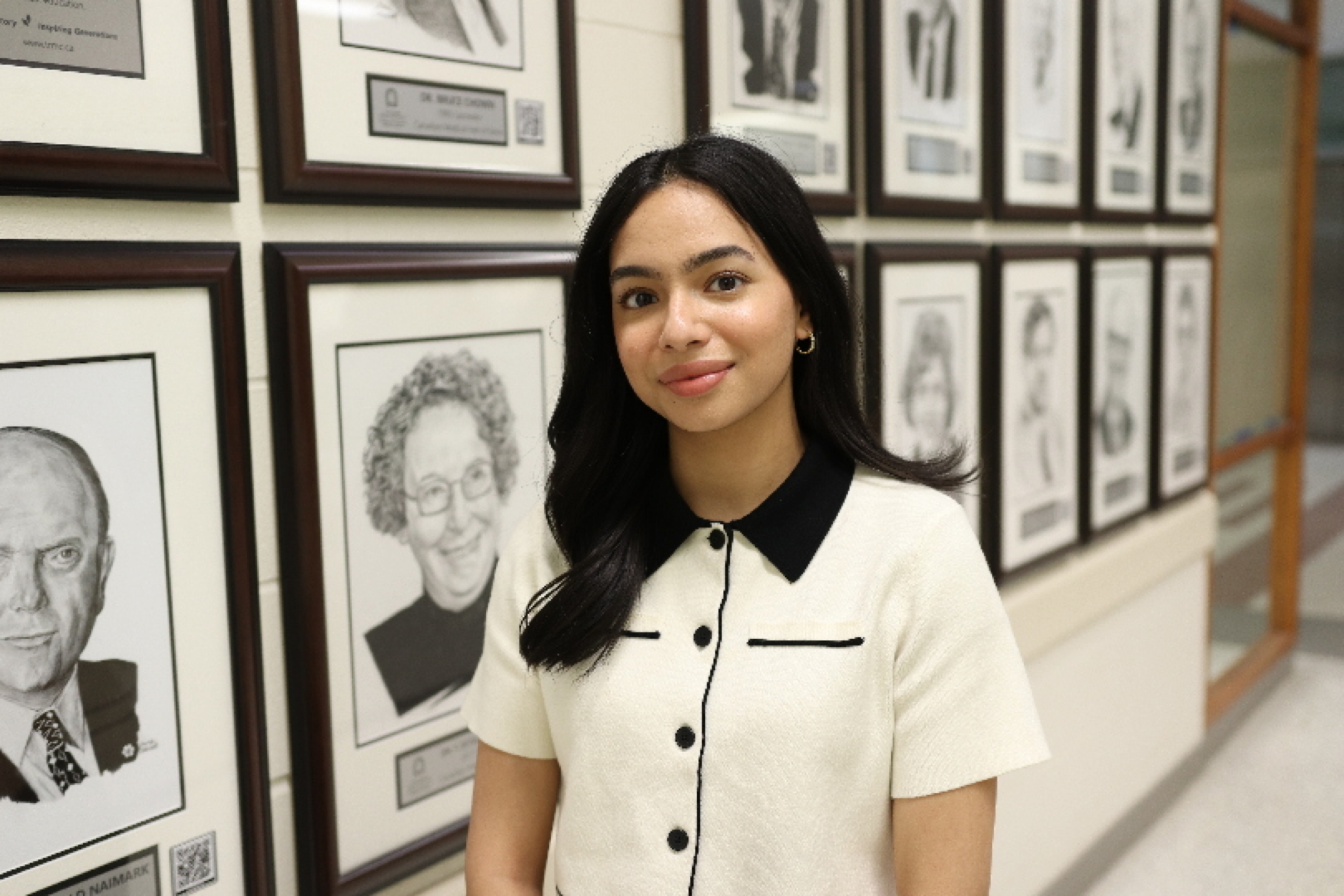Portrait of Tooba Razi in front of framed drawings of UM Canadian Medical Hall of Fame laureates.