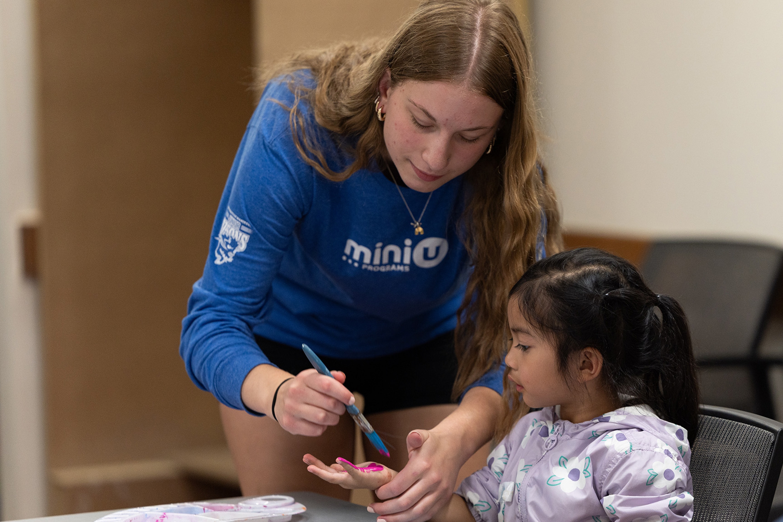 A Mini U leader working with a camper during an arts and crafts program.