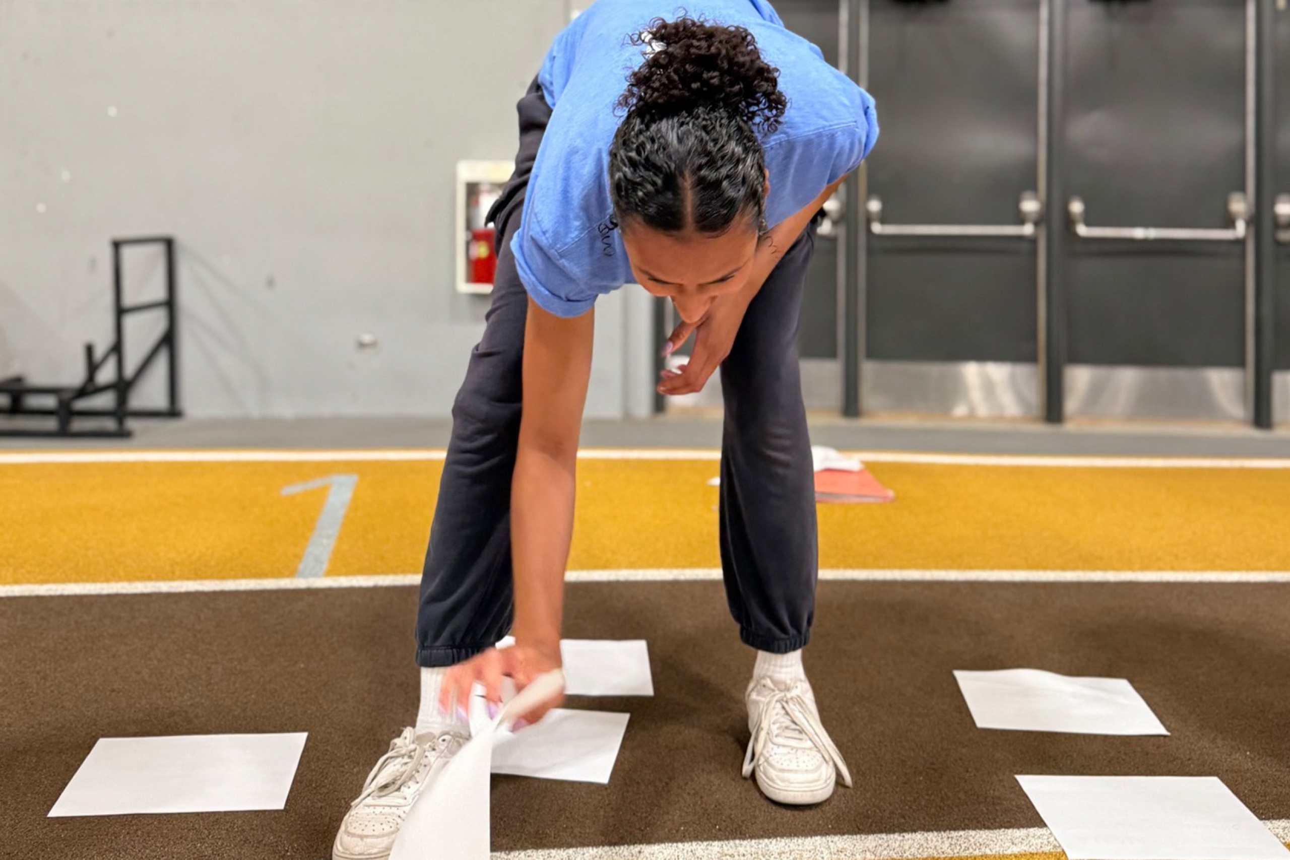 A Mini U leader in training bends over a an array of paper laid out on the track in the James Daly Fieldhouse.