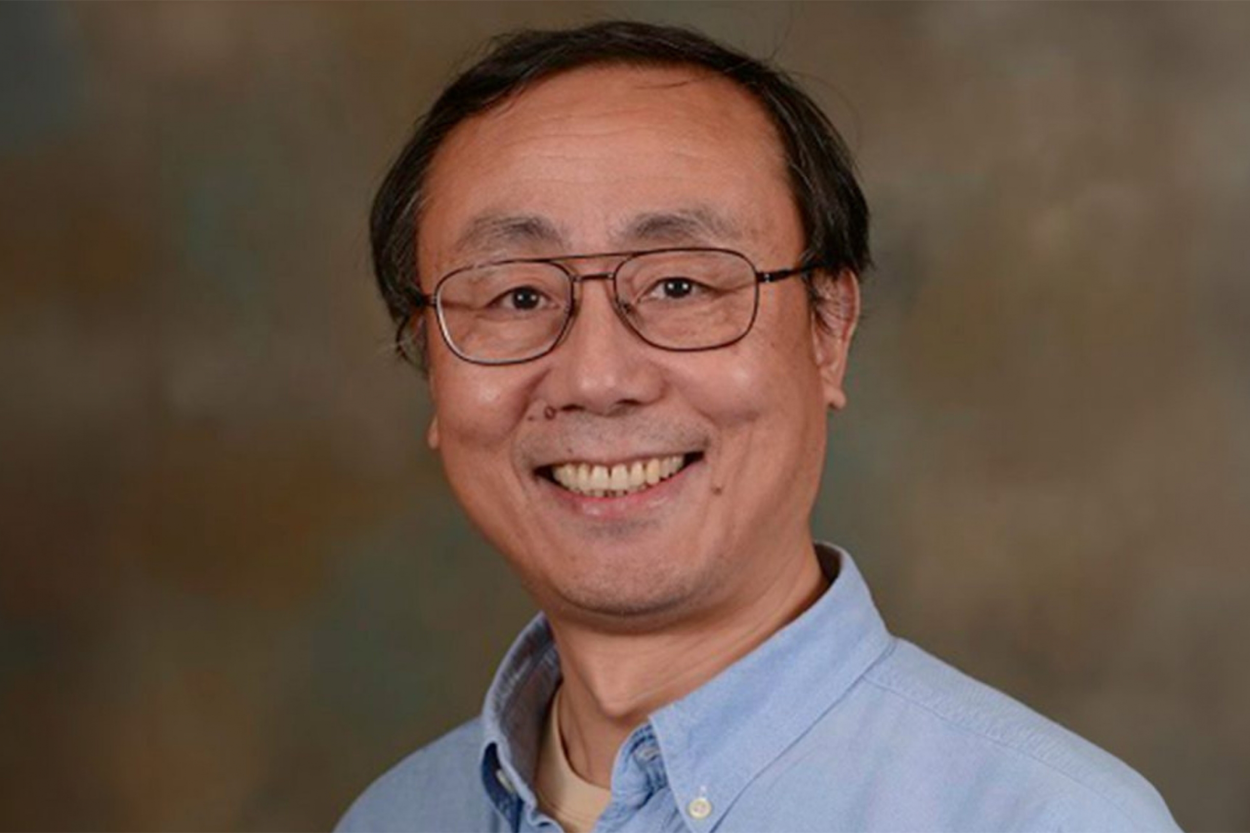 Can-Ming Hu wearing a blue collared shirt and an eyeglass smiling at the camera.