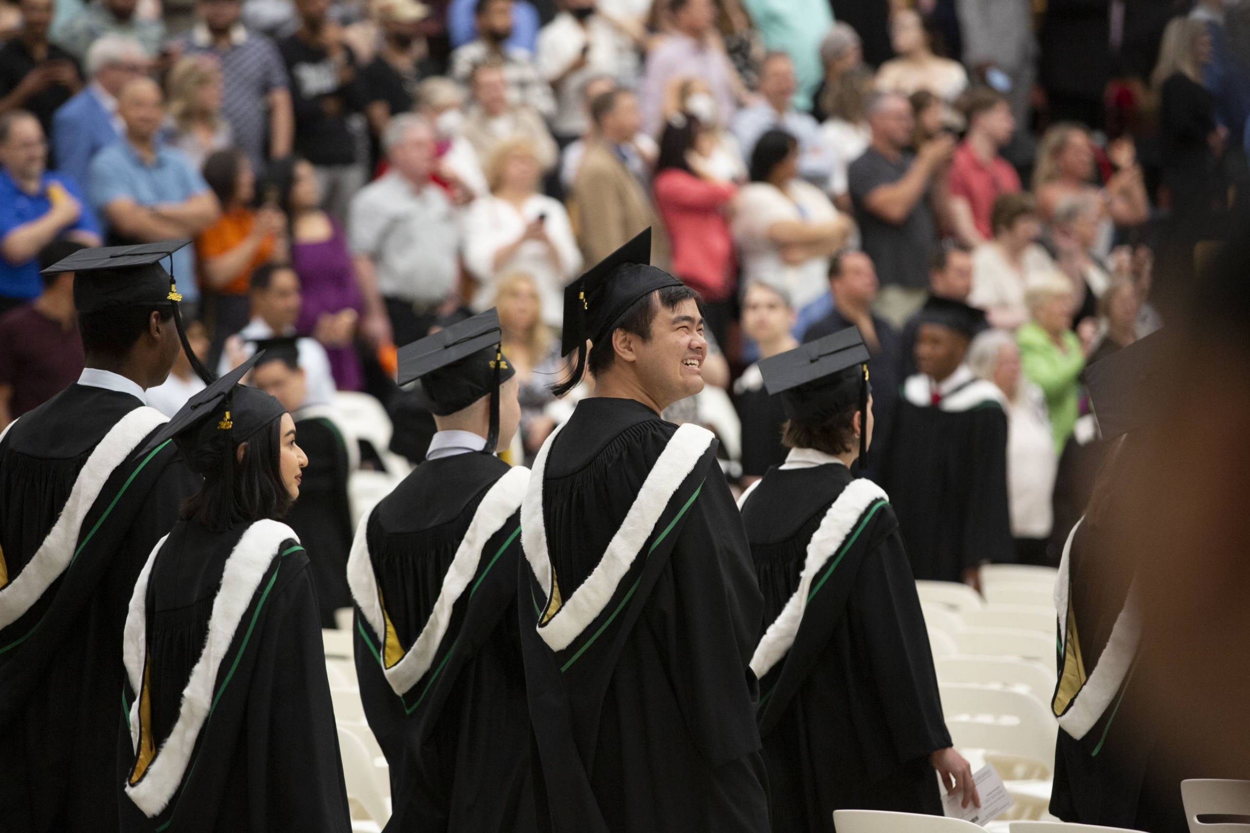 A graduate at convocation looking over their shoulder and smiling at the crowd. 