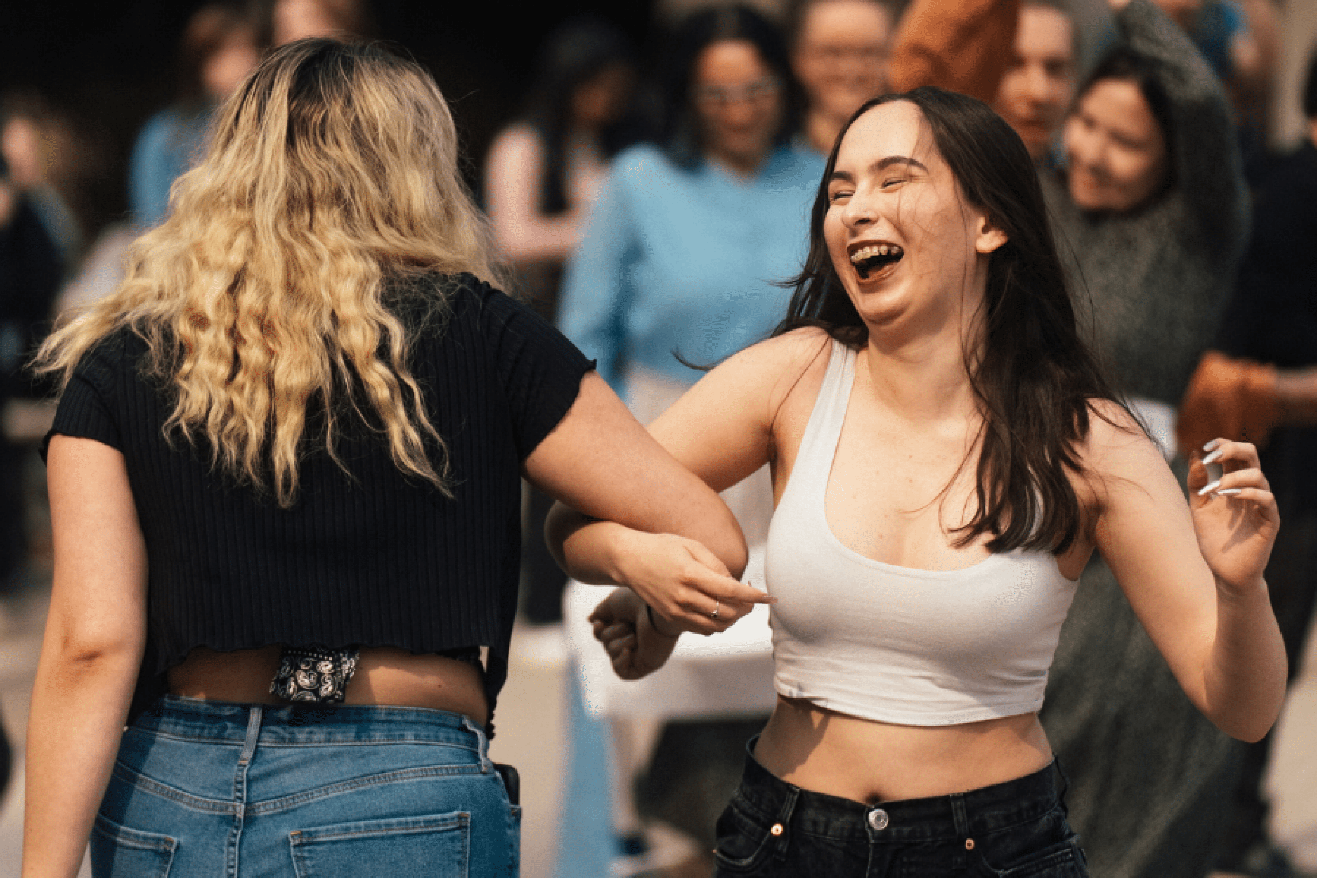 Two people laughing and dancing together at an outdoor gathering.