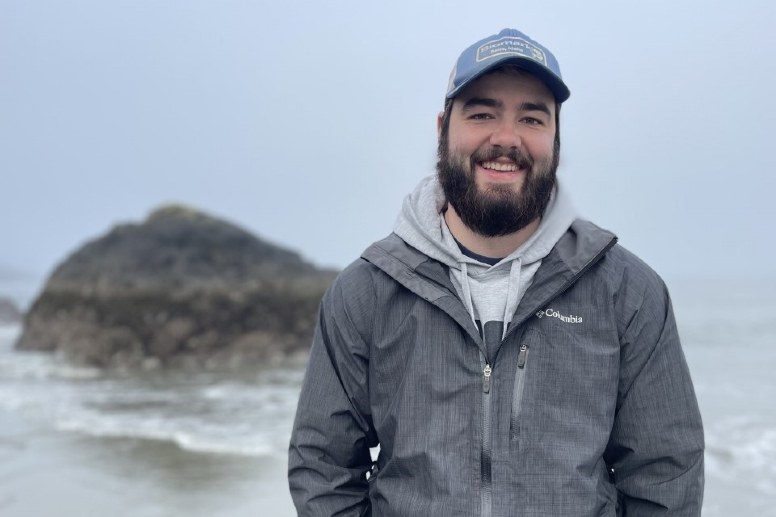 Smiling student poses for the camera infront of a ocean scene.