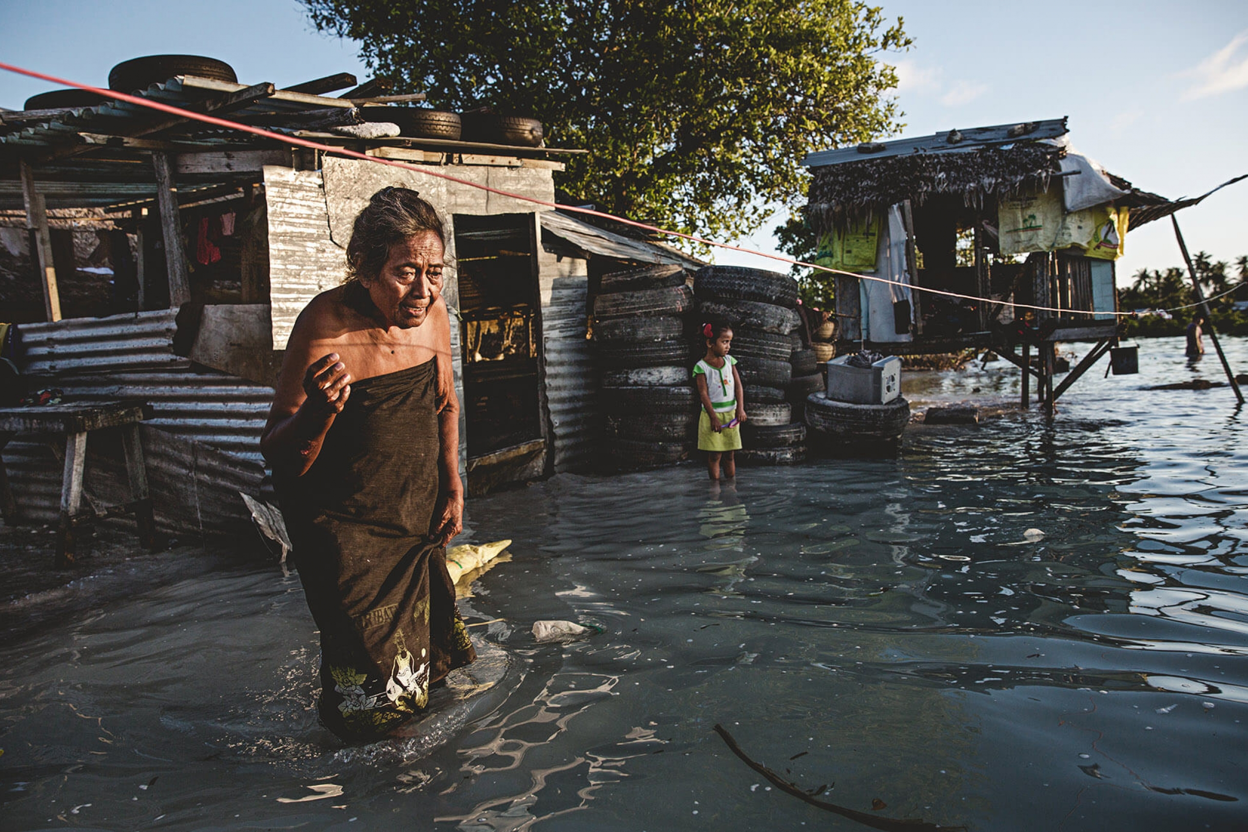 An elderly woman wades through knee-high sea water that flooded her house and village in Kiribati