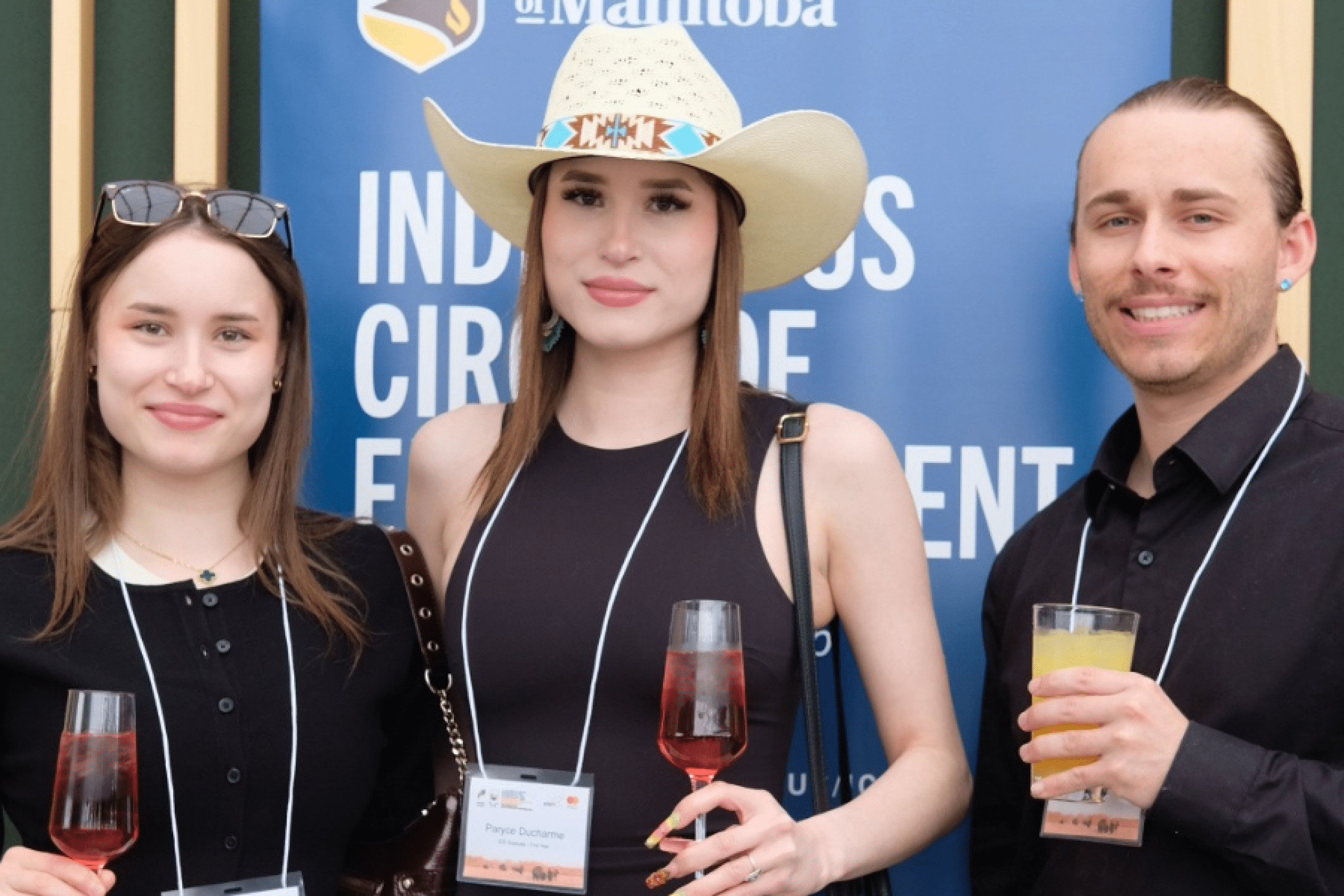 Three students hold drinks and pose together in front of an Indigenous Circle of Empowerment banner.