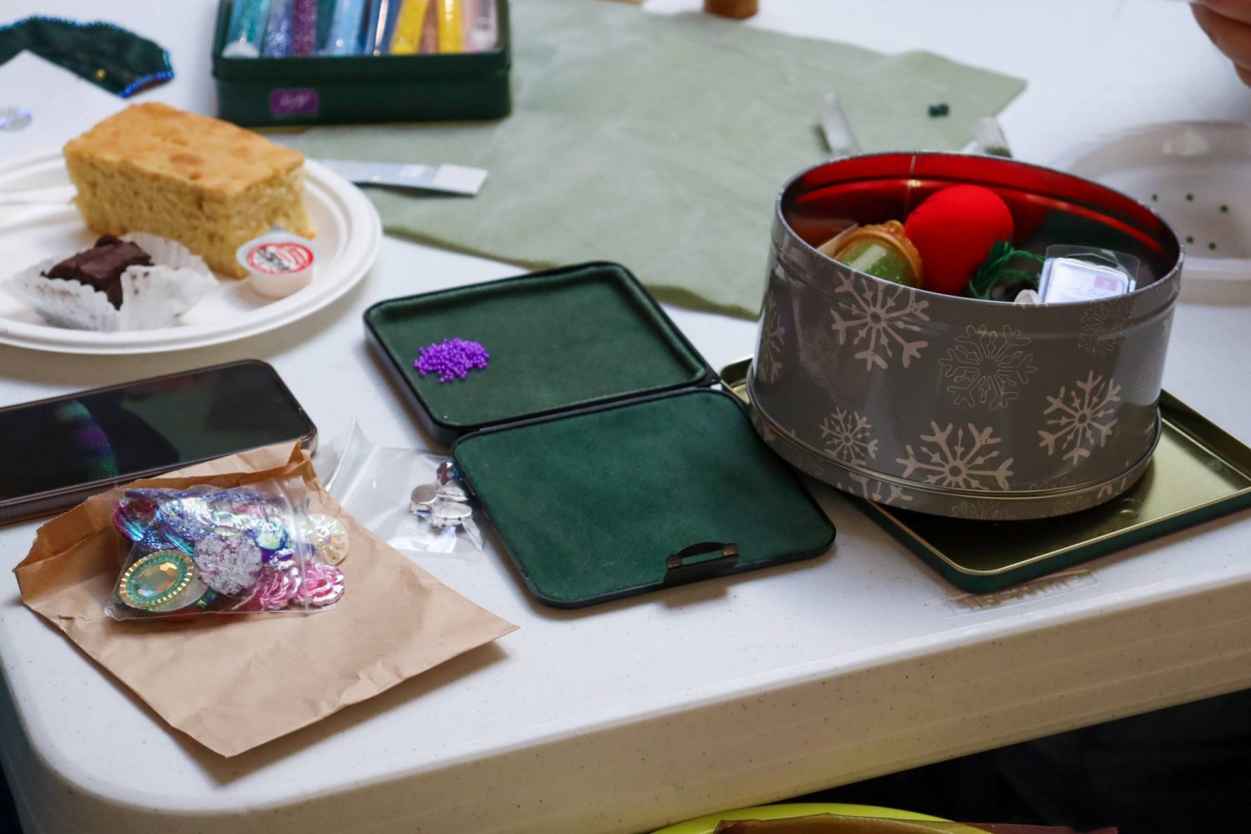 Close-up of a table with snacks and craft materials, including beadwork pieces, small trays, and a tin of supplies.