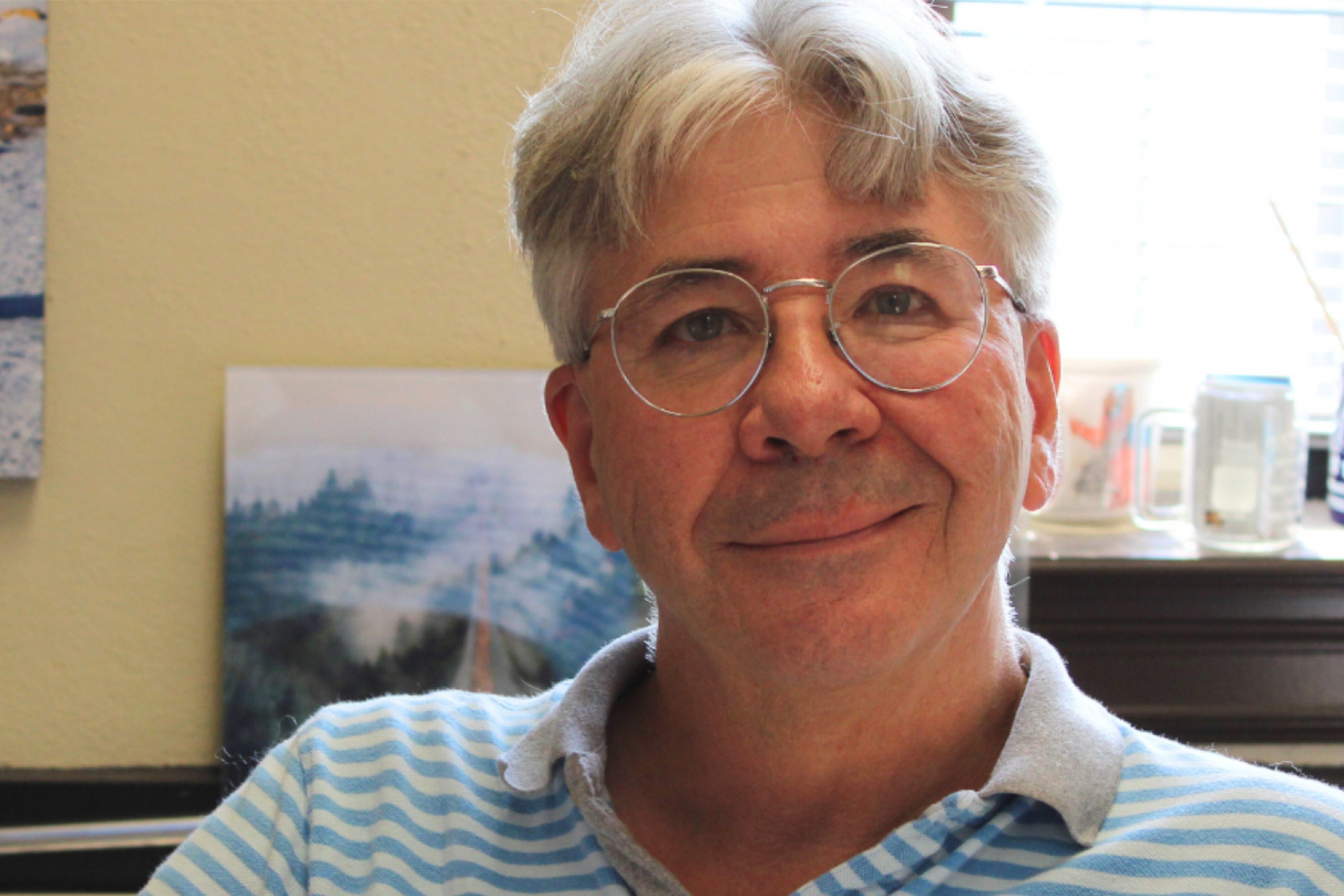 Ivan Oresnik wearing a stripe collared shirt and an eyeglass smiling at the camera.
