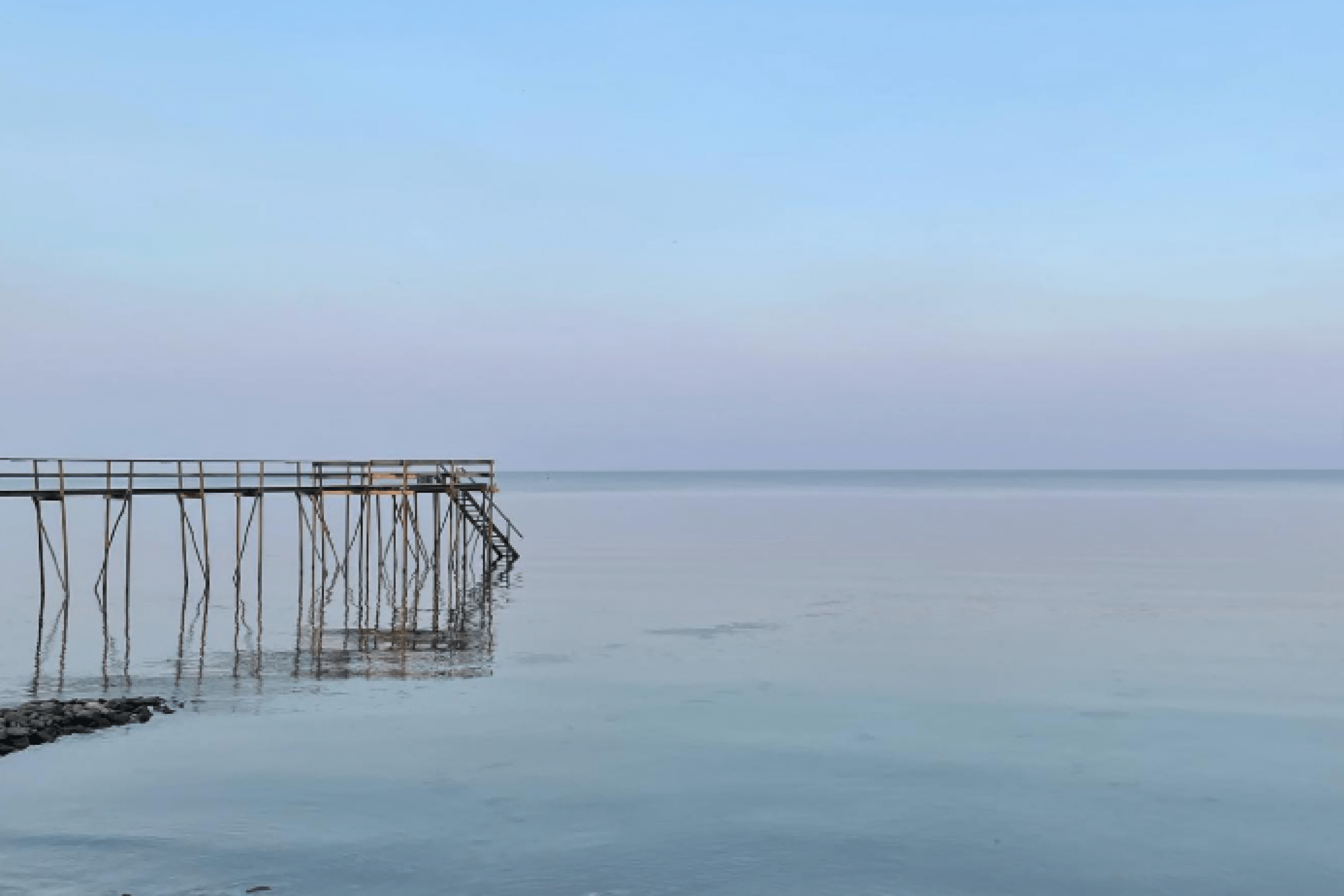 Pier jutting into calm Lake Winnipeg with blue sky.
