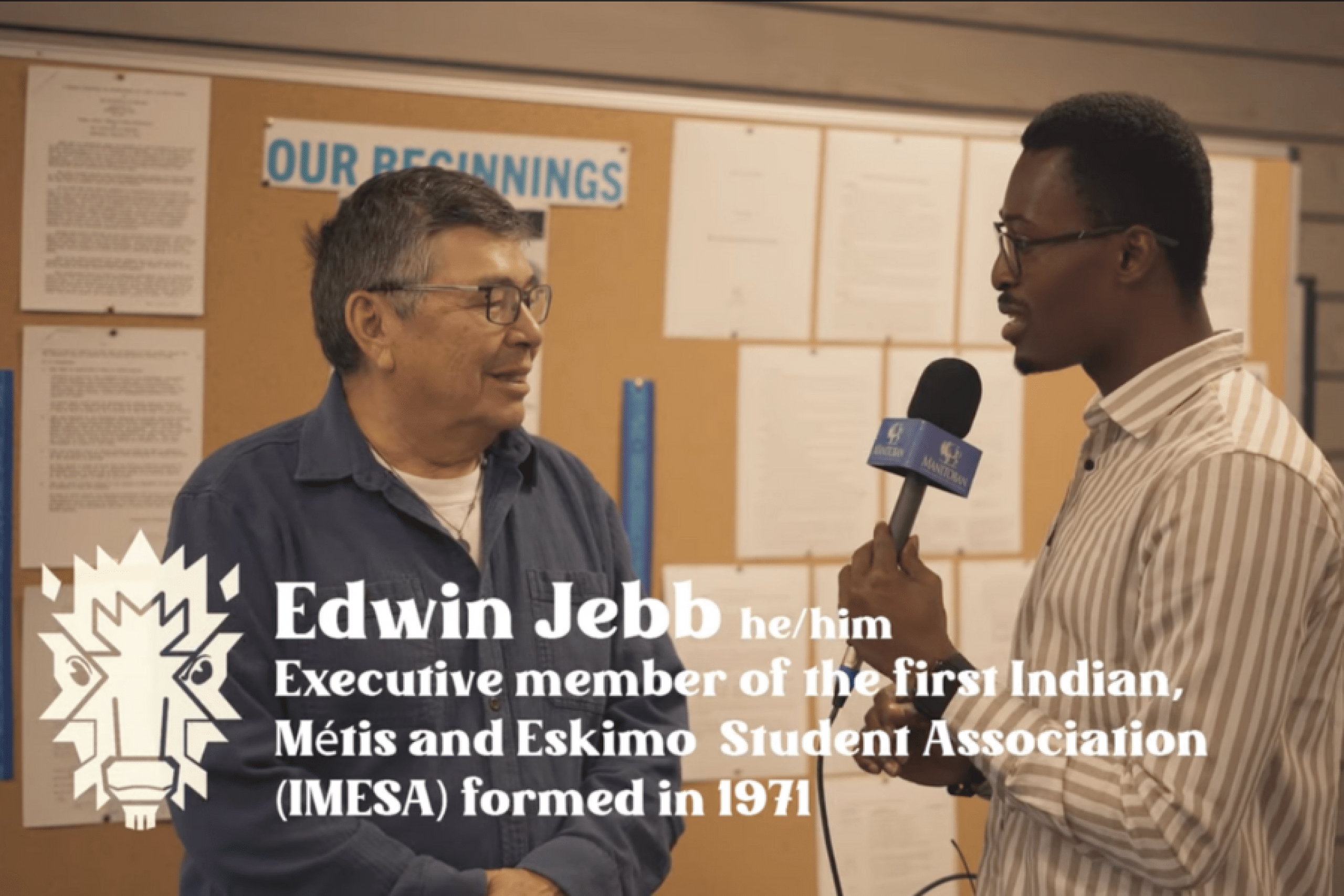 An interviewer speaks with Edwin Jebb in front of a bulletin board during an Indigenous student history feature.
