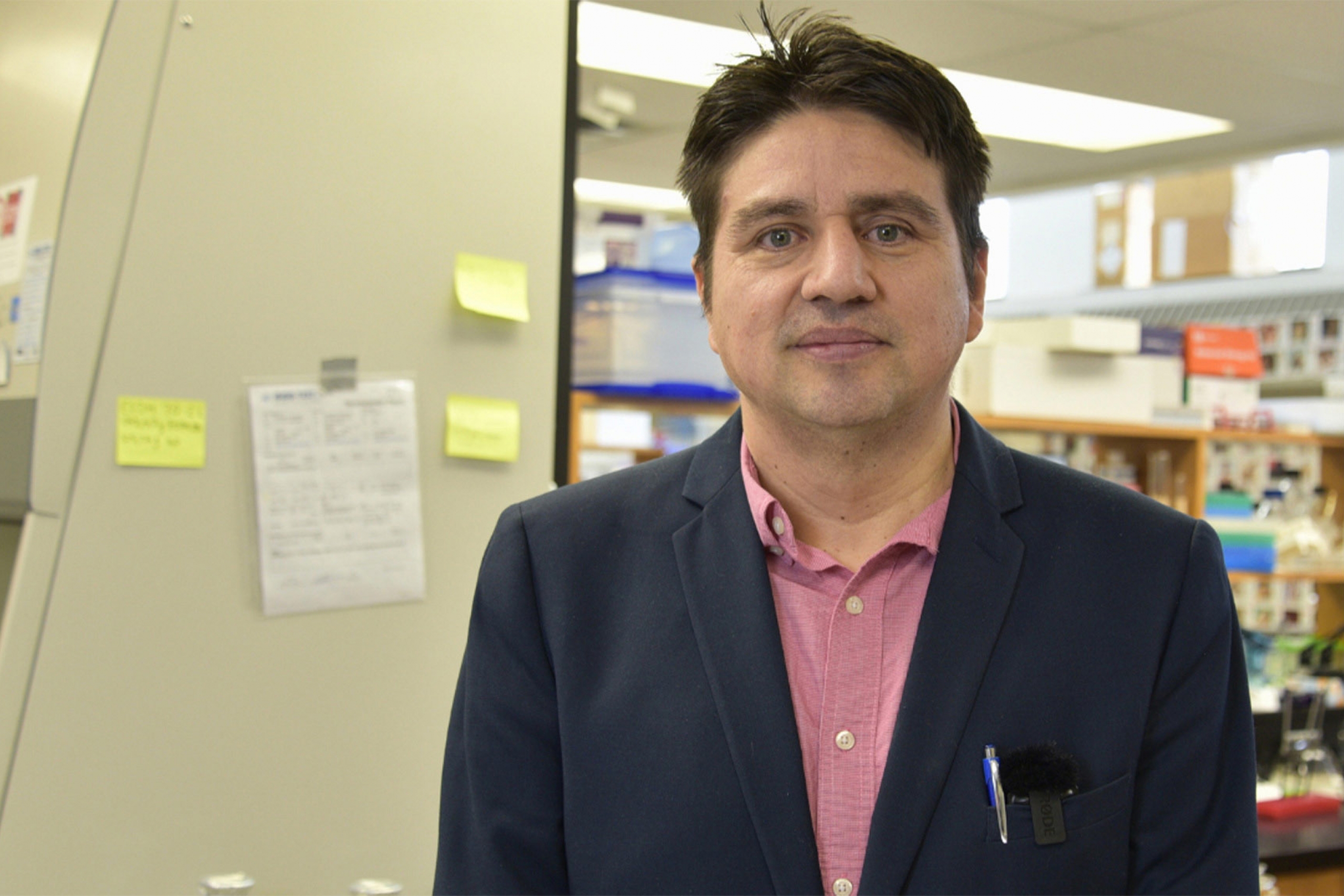Miguel Uyaguari-Diaz wearing a pink button down shirt with a coat smiling at the camera.