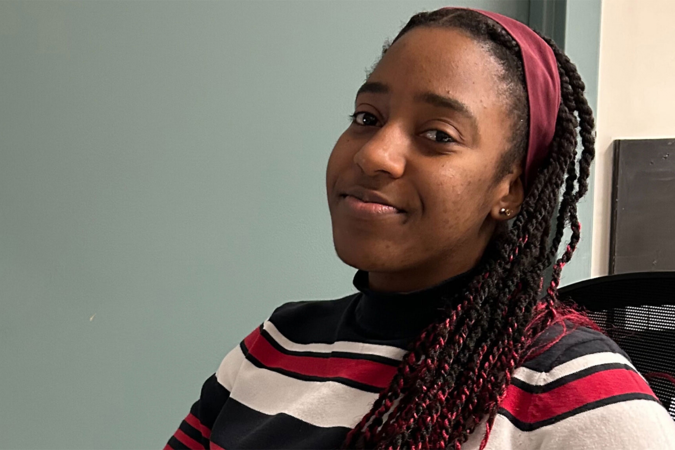 Munashe Nhunzwi wearing a stripes top and a red head band smiling at the camera.