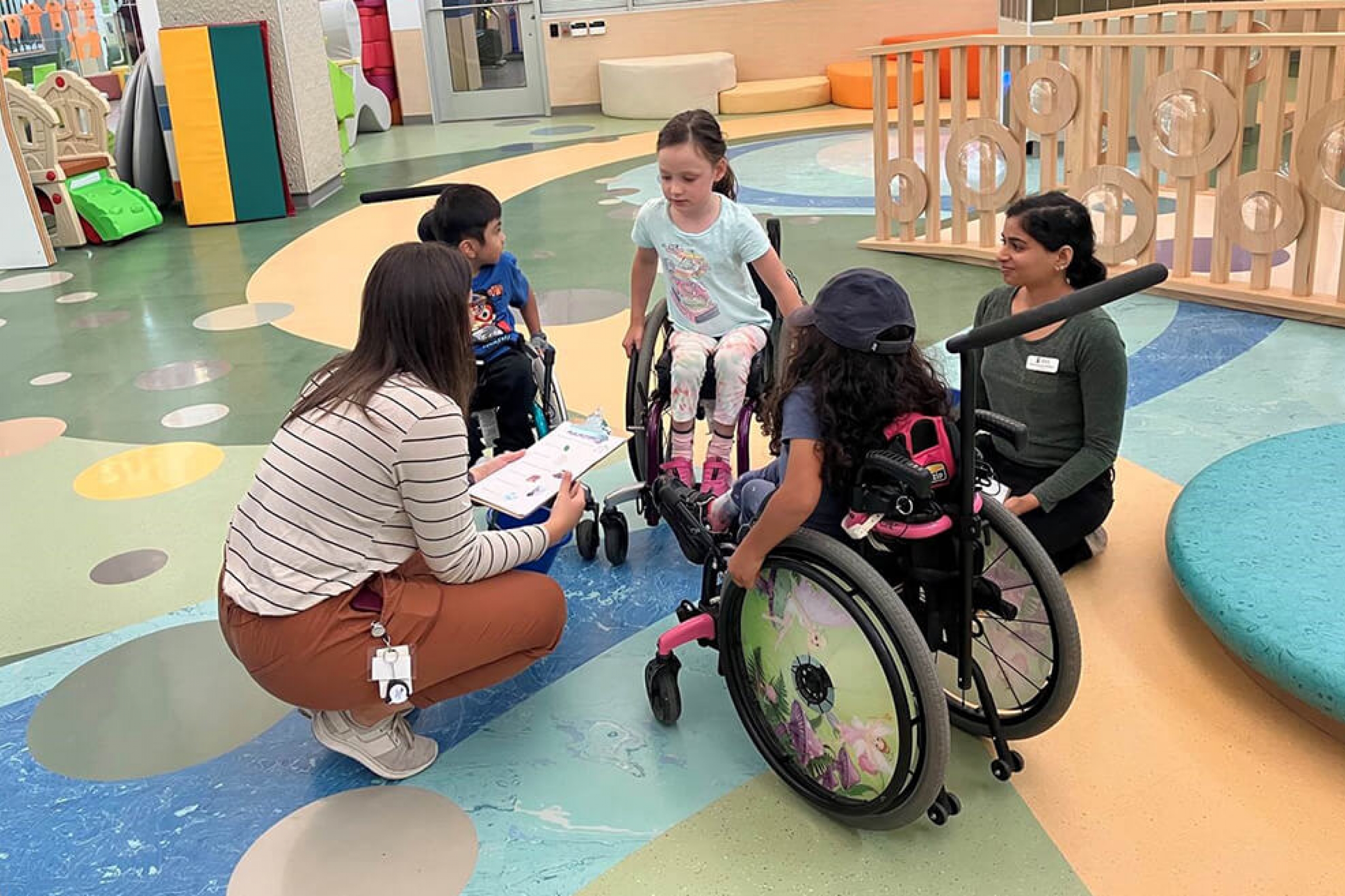 Three children in wheelchairs in a circle with two occupational therapy students.