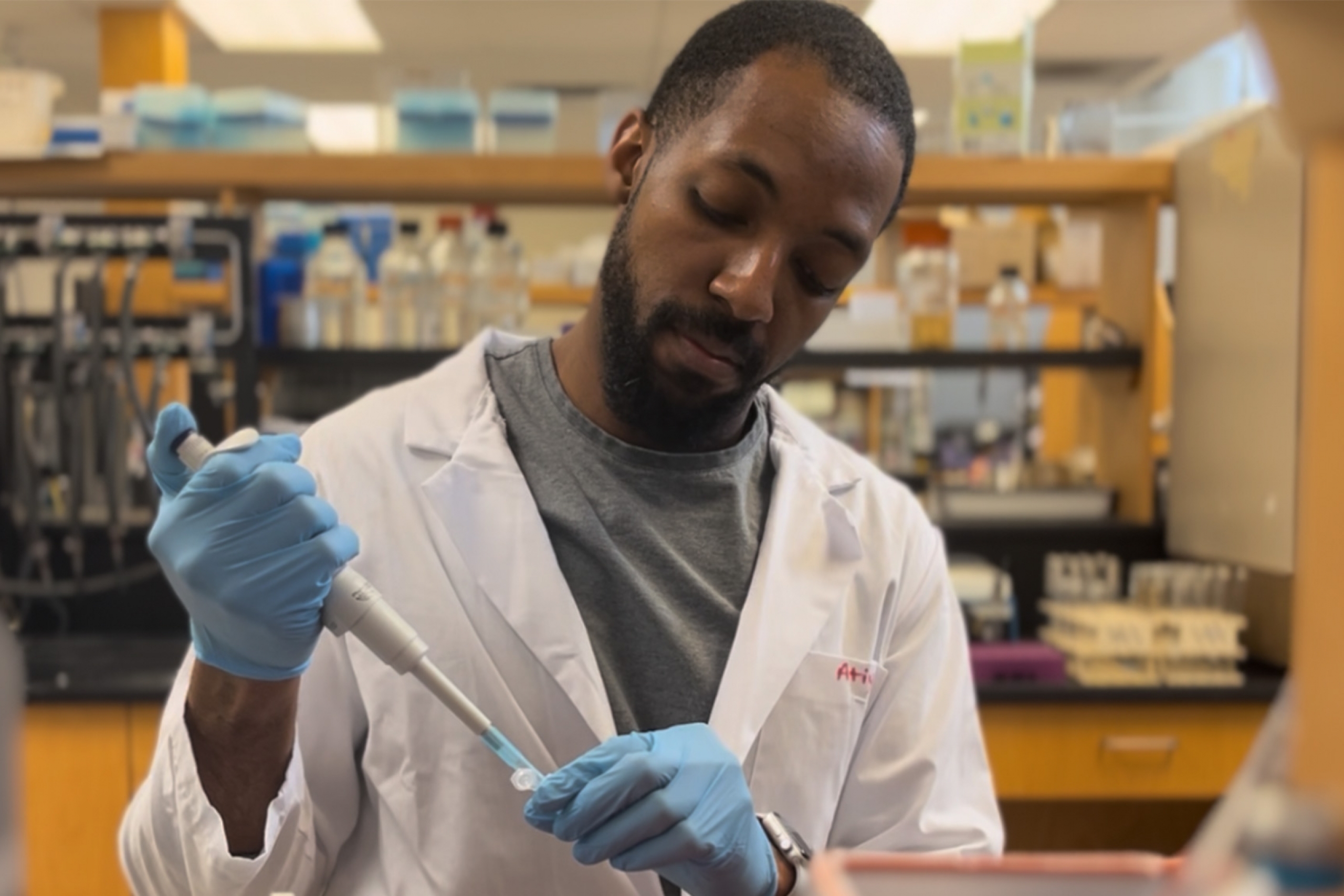Steve Daley wearing a gloves and lab coat pipetting.