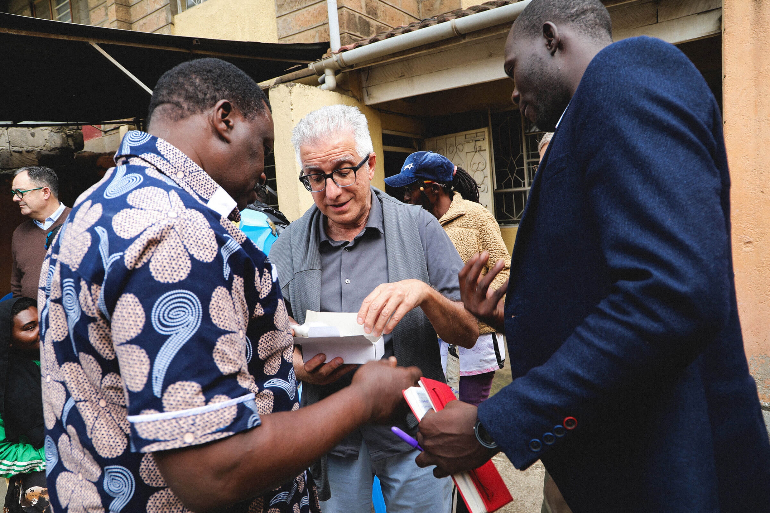 Three men stand together looking at a box of medical supplies
