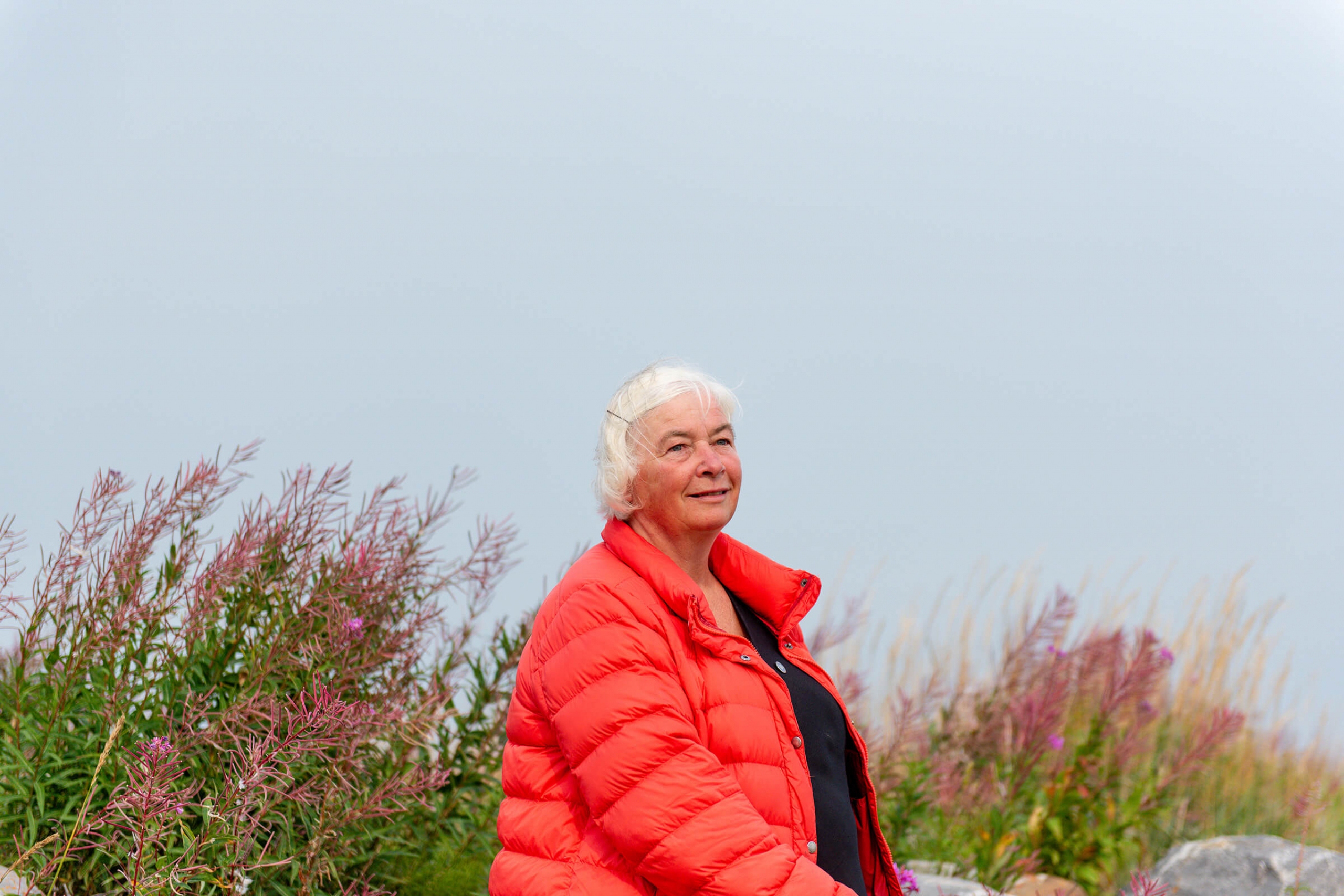 A smiling woman in an orange coat with wild grasses in the background