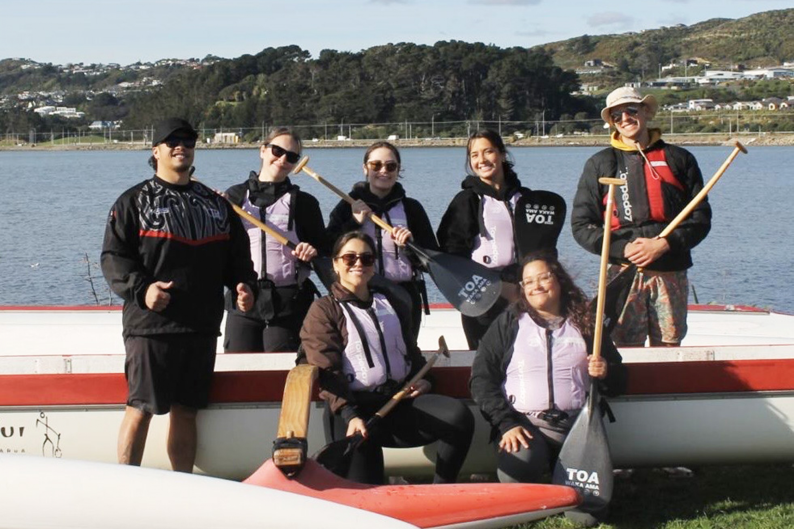 A group of people pose by a canoe near a lake.