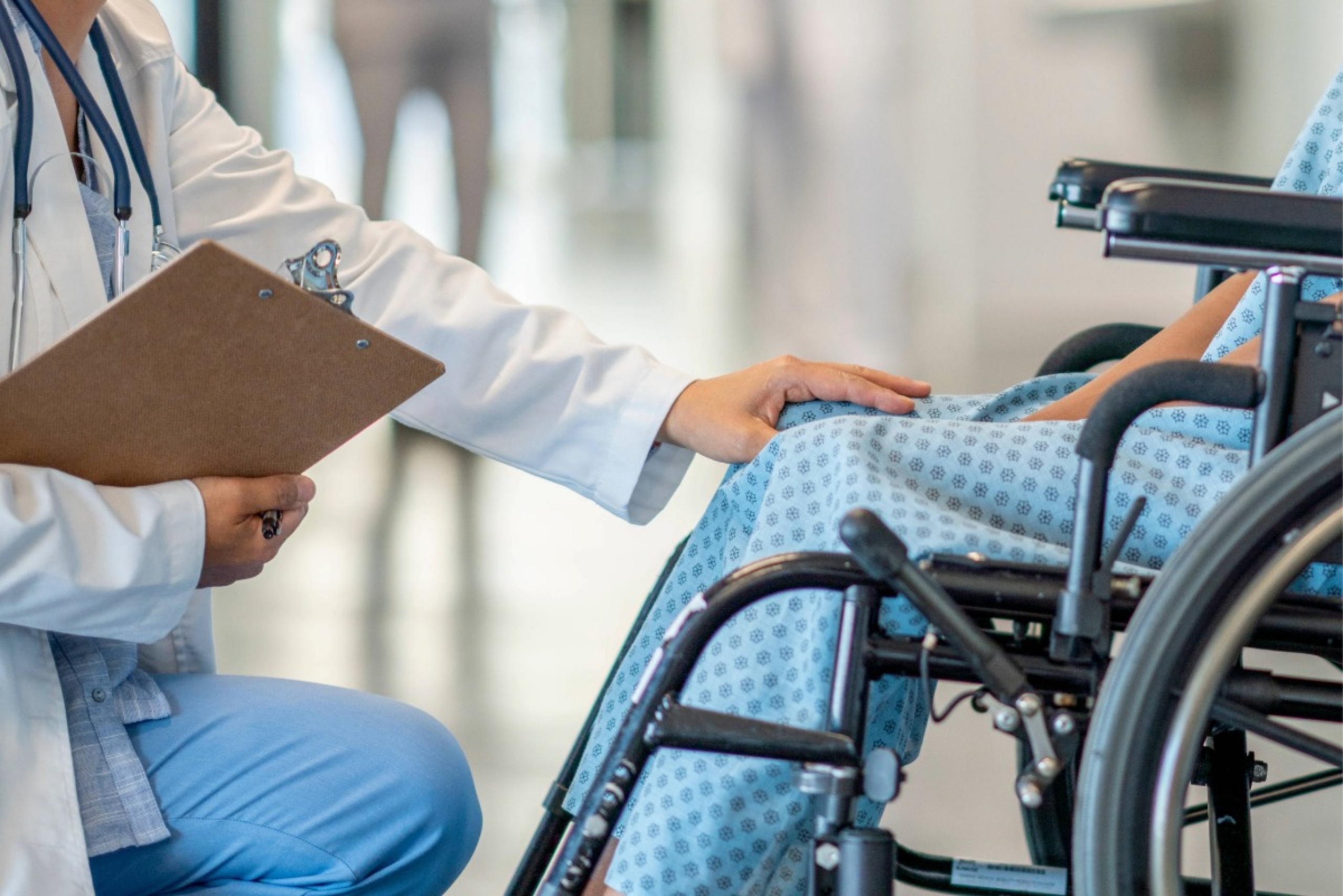 A patient sits in a wheelchair and is helped by a doctor who approaches patient in an empathetic way.