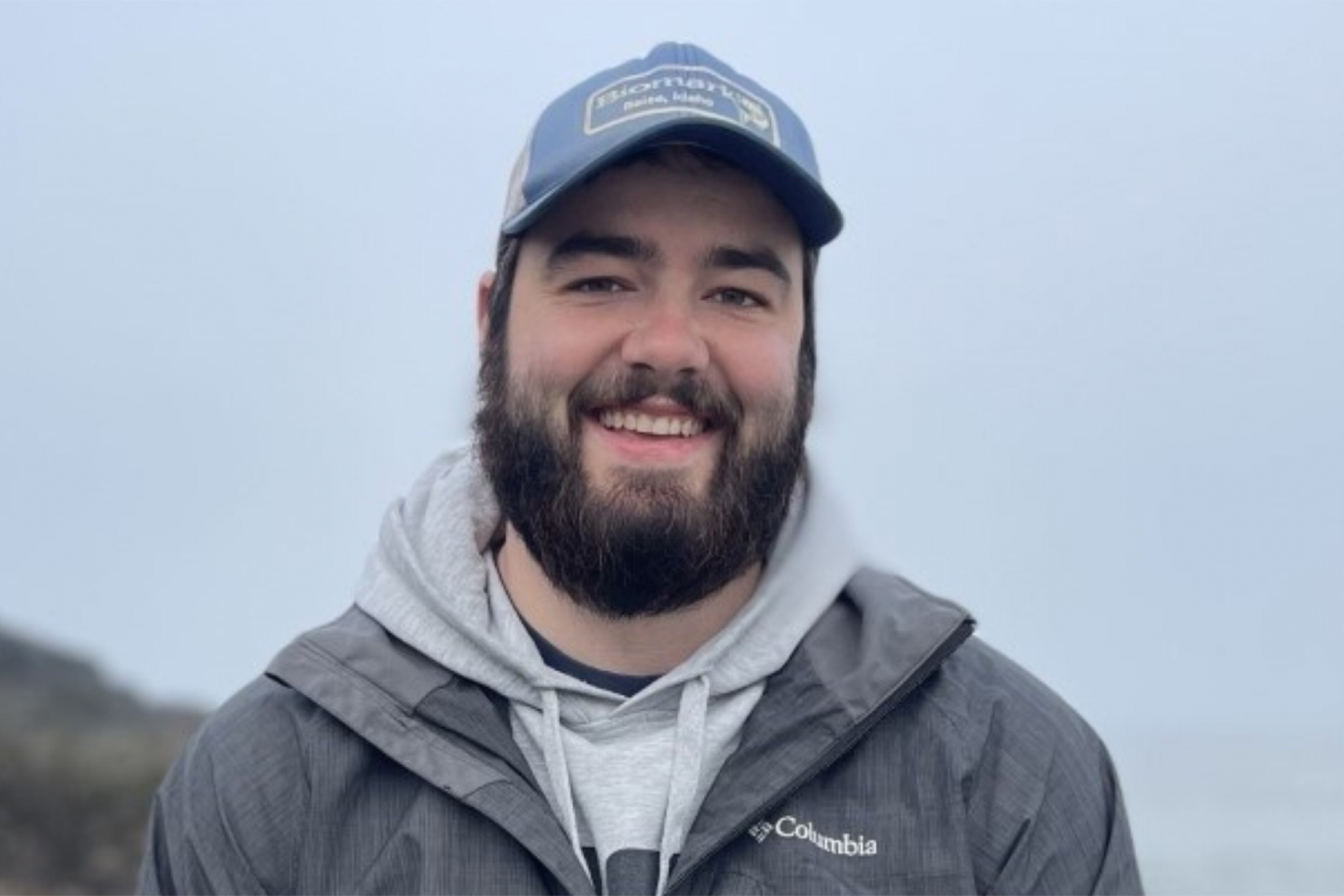 Will Bugg wearing a gray hoodie and jacket with a cap smiling at the camera.