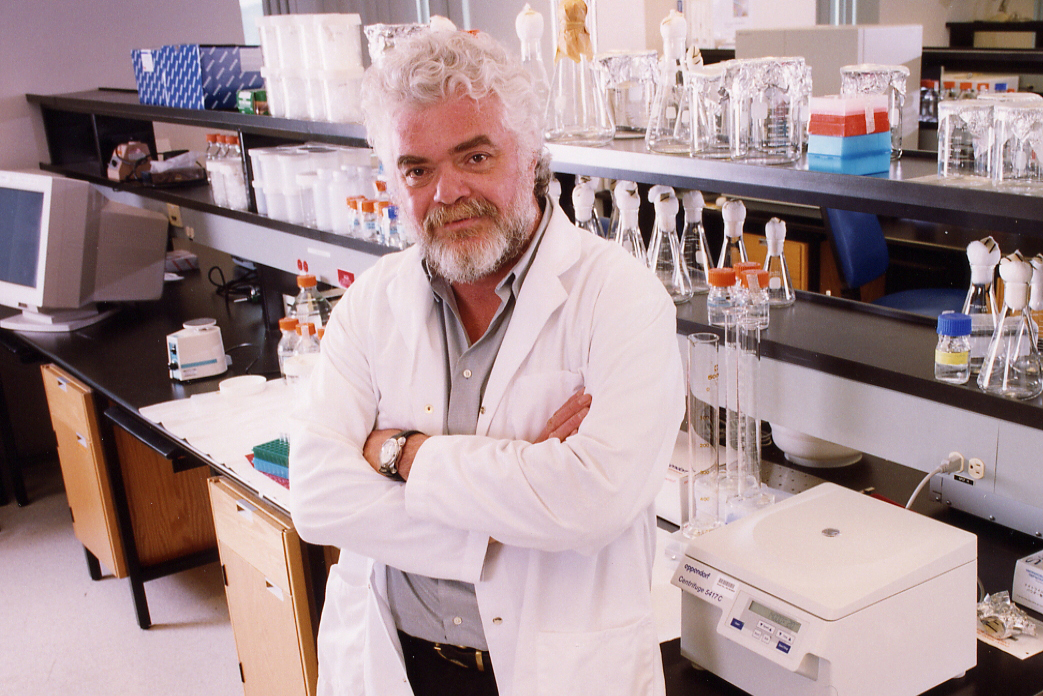 Dr. Frank Plummer poses for the photo in a lab. He is wearing a white coat.