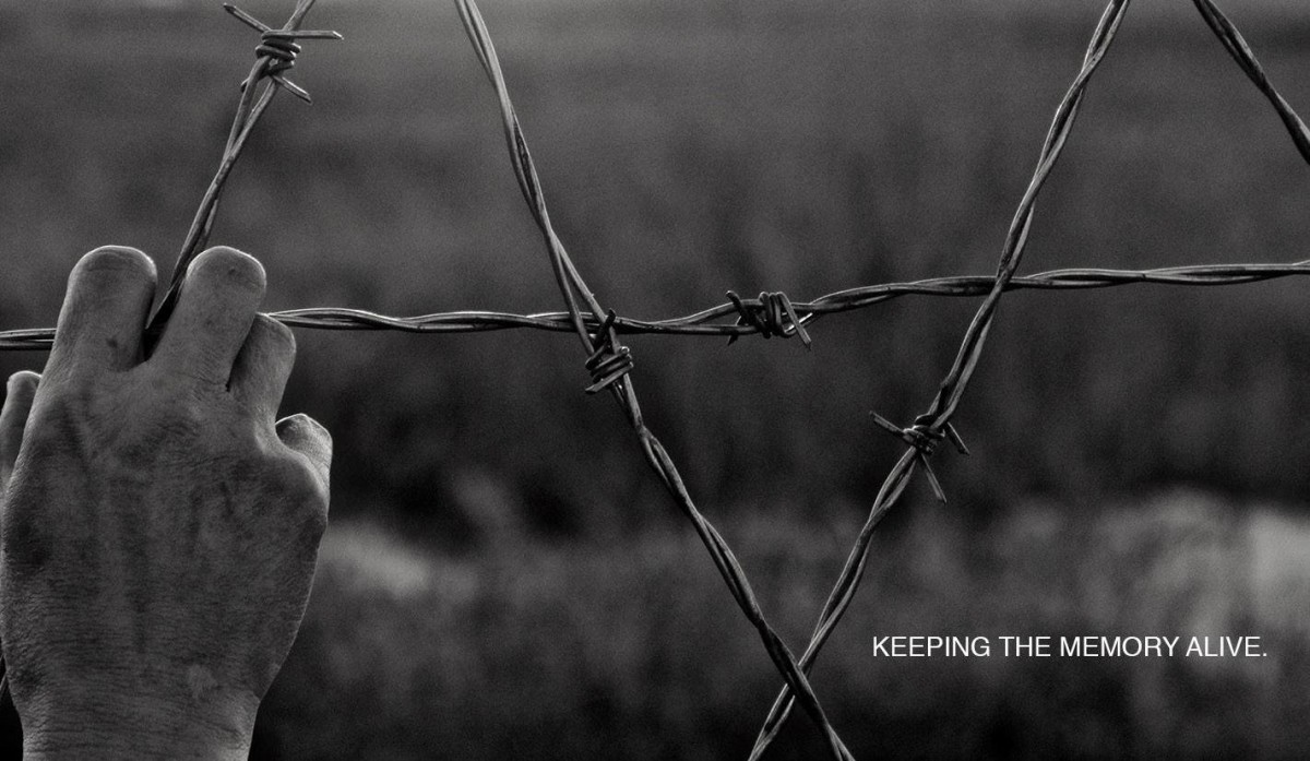 A hand gripping barbed wire fence with teh words "keeping the memory alive"
