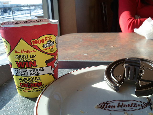A Tim Hortons paper coffee cups sits next to an empty plate