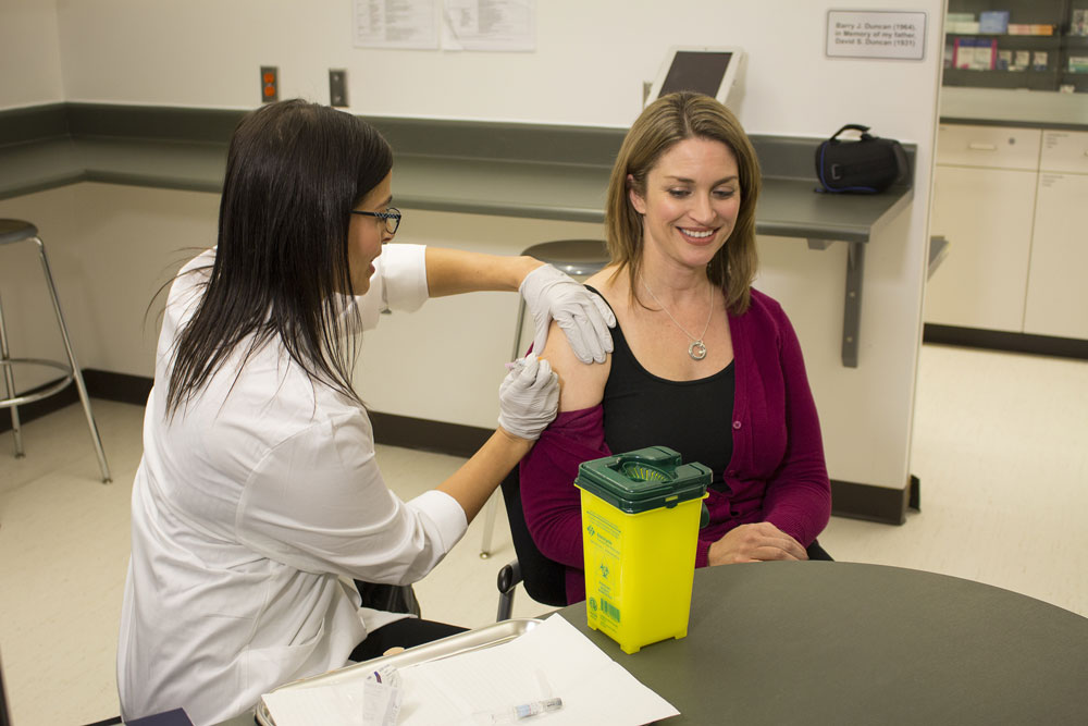 Health Minister Erin Selby receives a flu shot administered by Dinah Santos, a certified pharmacist and instructor (College of Pharmacy).