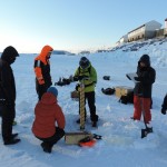 A student in the field school coring the sea ice, while other students record basic measurements of the sea ice.