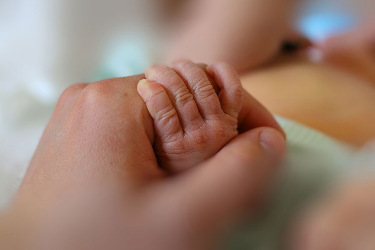 Adult holds newborn baby's hand. // Image from iStock.