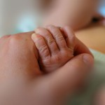 Adult holds newborn baby's hand. // Image from iStock.