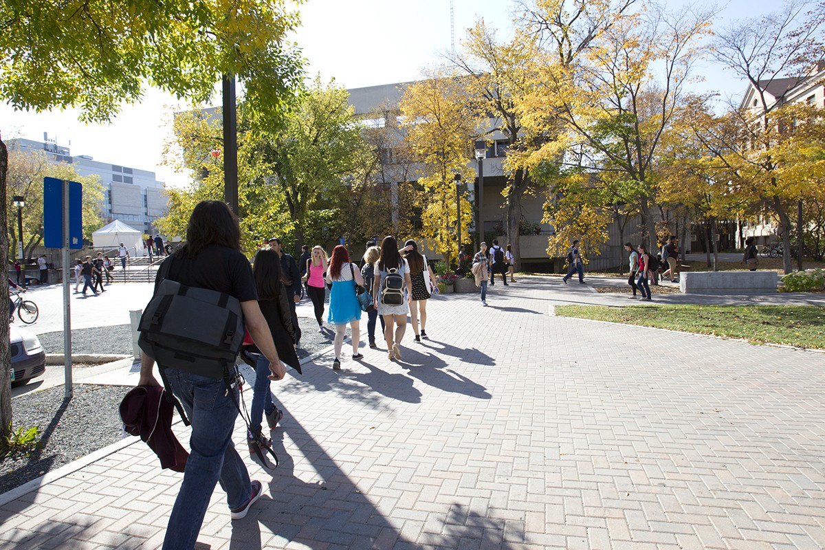 People walking on brick sidewalk with autumn trees in the background.