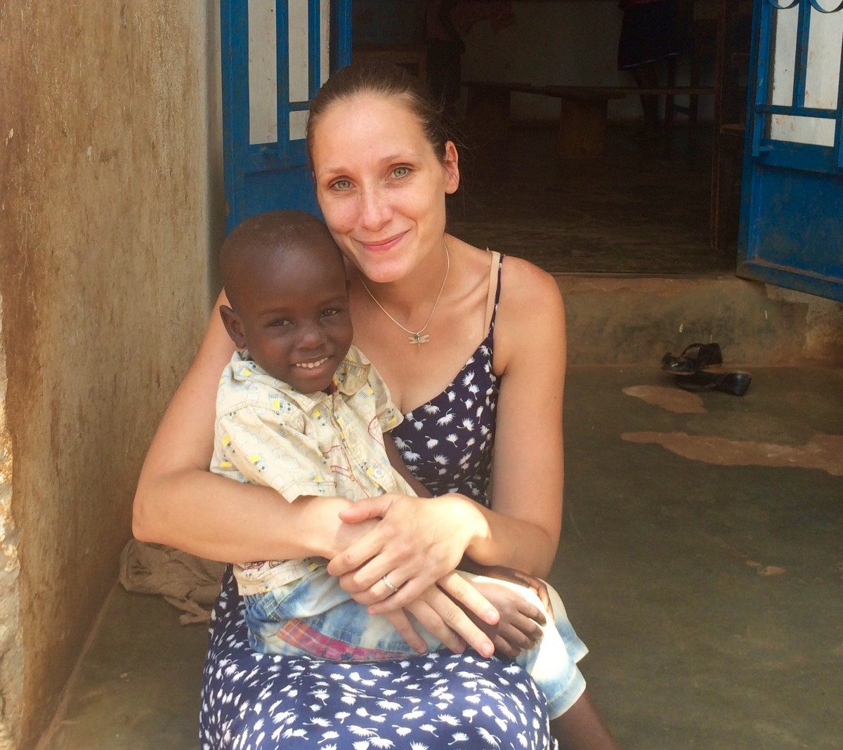 Lindsay Aboud is seated, holding a village boy on her lap in Uganda.