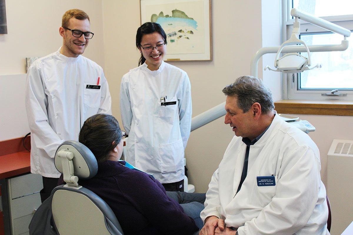 DENTISTRY STUDENTS JOHN HART (L) AND LAN LI CONFER WITH DR. REYNALDO TODESCAN AND A PATIENT.