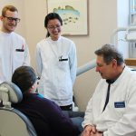 DENTISTRY STUDENTS JOHN HART (L) AND LAN LI CONFER WITH DR. REYNALDO TODESCAN AND A PATIENT.