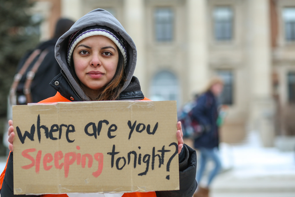 A girl holds up a sign asking "where are you sleeping tonight?