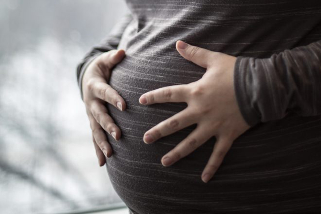 Closeup of a pregnant woman's belly, with both hands on belly.