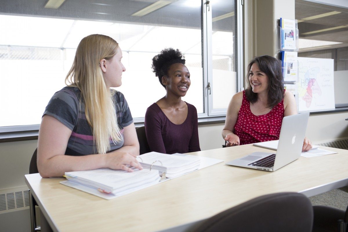 Three people sit around a table working on resumes