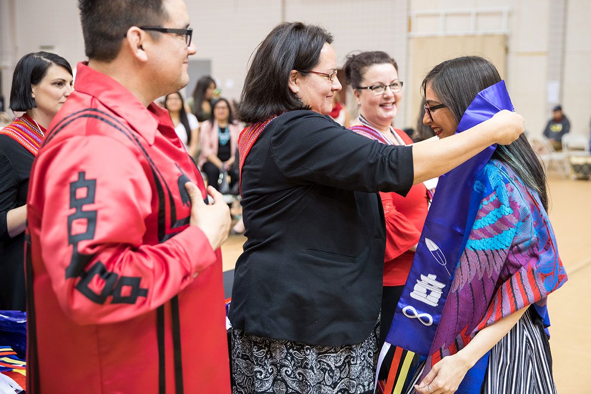 Frank Deer, Acting Executive Lead, Indigenous Achievement, and Christine Cyr, Director of the Indigenous Student Centre, present recent graduate Kristin Flattery [BFA (Hons)] with a purple scarf at the 28th Annual Graduation Pow Wow.