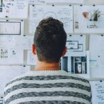 you seethe back of a man's head as he stares at a bulletin board ful of papers