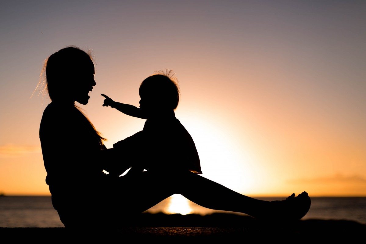 Mother and child playing and watching sunset in silhouette