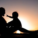 Mother and child playing and watching sunset in silhouette