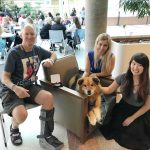 Rusty the dog sits on a chair with students smiling by him