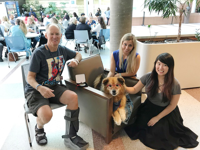 Rusty the dog sits on a chair with students smiling by him