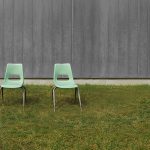 Two empty chairs in front of a wall, outdoors.