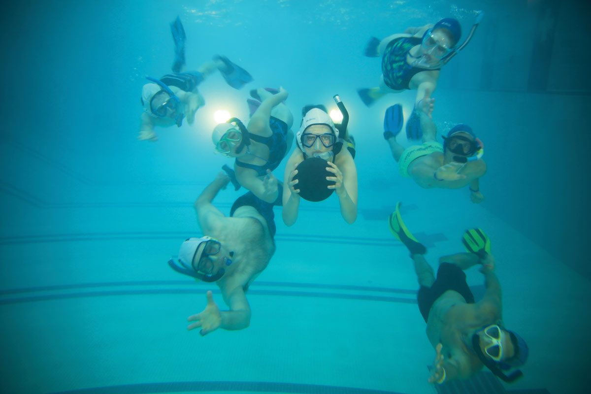 Swimmers wearing goggles and snorkels play with a ball underwater. // photo by Mike Latschislaw