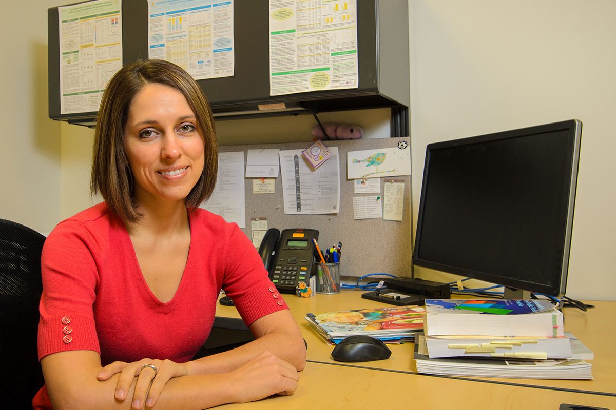 Meghan Azad, UM researcher in pediatric health sits in an office at a desk next to a computer.