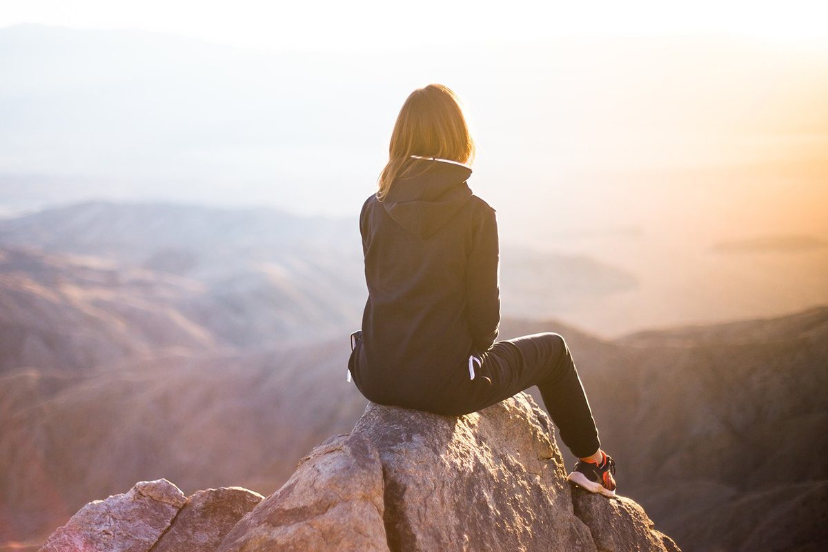 Woman looks at sky from a mountain top. // Image from Pixabay.